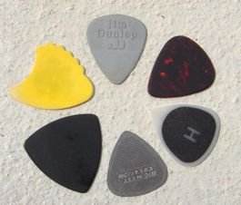 Various guitar picks. From top going clockwise: A normal plastic pick; An imitation tortoise-shell pick; A plastic pick with high friction coating (black areas); A stainless steel pick; An equal-sided pick; and a "shark's fin" pick